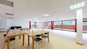 Ein Konferenzraum mit großen Fenstern, einer weißen Decke und einem Holztisch mit Stühlen.