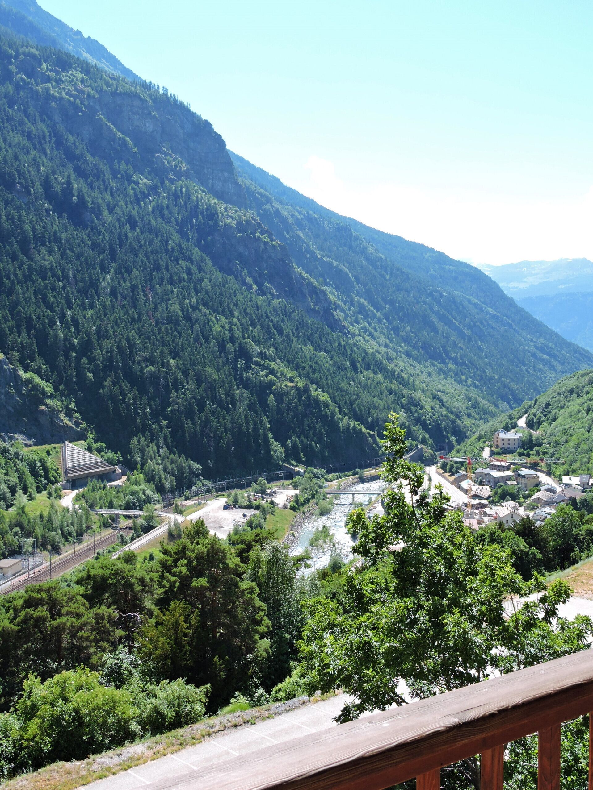 A mountainous landscape with a river, a bridge, and a small settlement with buildings and a train track.