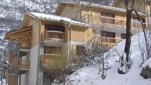 Eine Holzhütte mit Steinunterbau, mehreren Balkonen und einer verschneiten Landschaft.