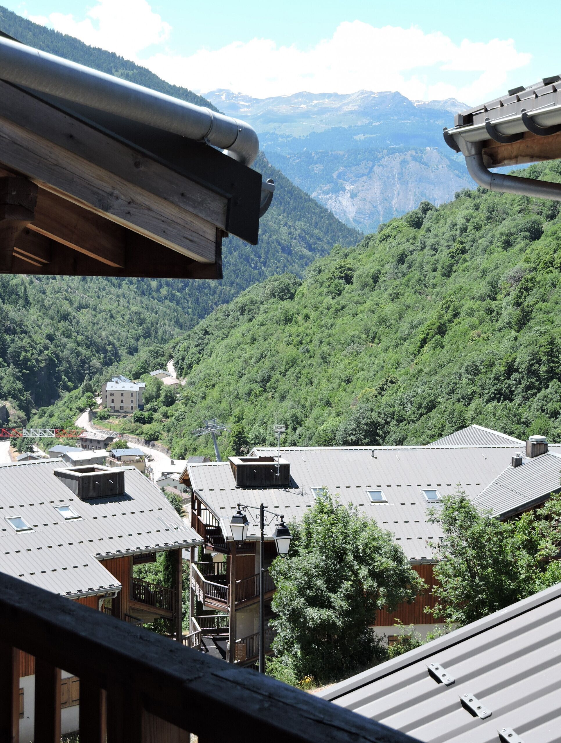 Un village de montagne aux bâtiments traditionnels en bois, avec un escalier en bois et une vue sur la forêt et les montagnes environnantes.