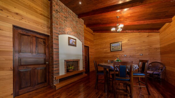 A wooden interior with a brick fireplace, wooden dining table, and chairs. - Hacienda Grande Hotel (San Cristóbal Totonicapán)