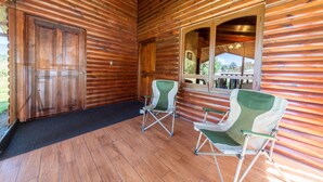 A log cabin with a wooden exterior, a large door, two folding chairs, and a window with a view of the outside. - Hacienda Grande Hotel (San Cristóbal Totonicapán)