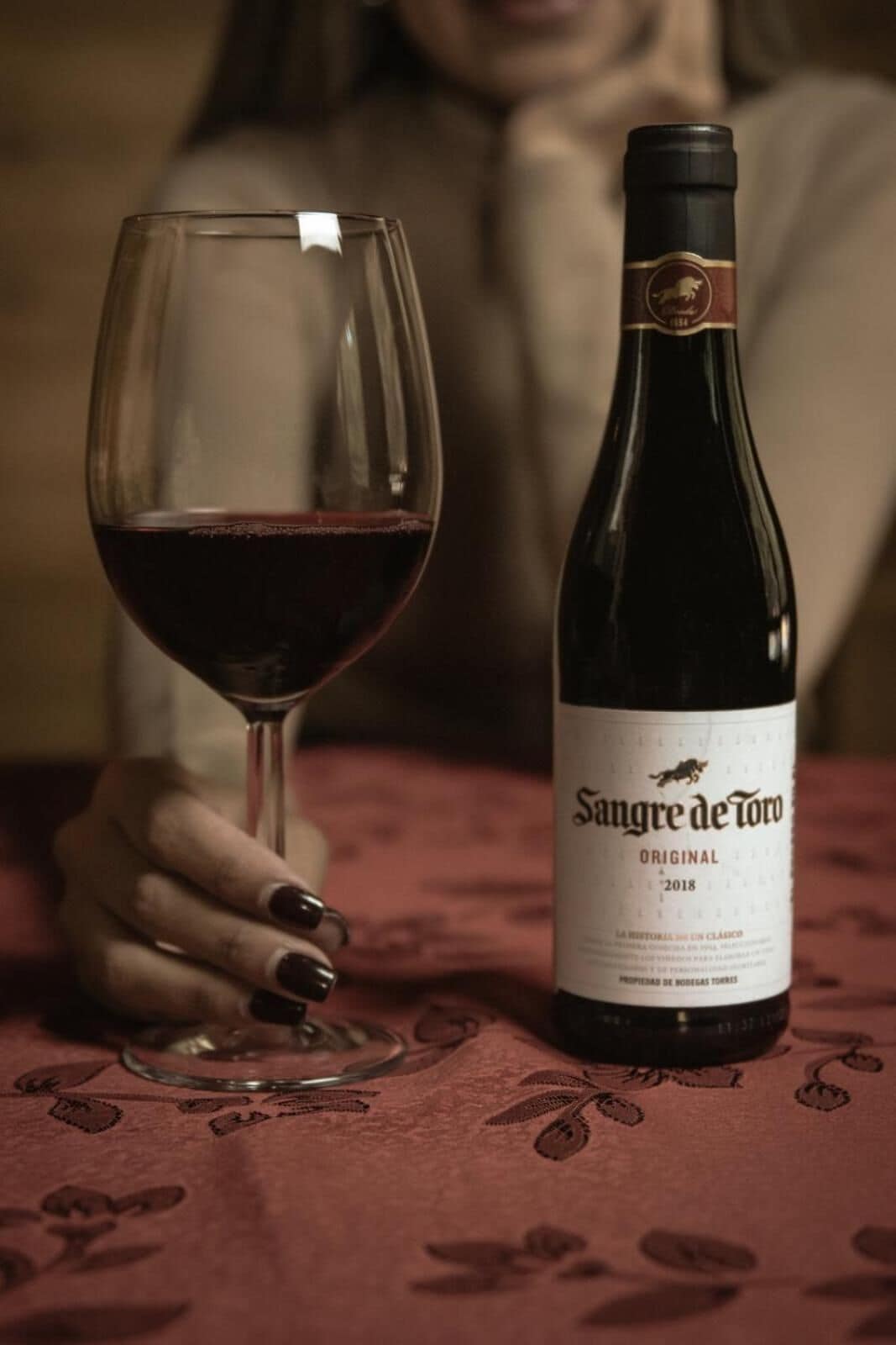 A bottle of Sangre de Toro wine and a glass of red wine on a table.