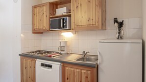 Kompakti keittiö, jossa on puukehikoiset kaapit, sisäänrakennettu mikroaaltouuni, astianpesukone ja jääkaappi.