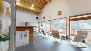 A spa area with wooden beams, a reception desk, and several lounge chairs with a view of a forested landscape. - Hameau 6 002 - SPA & PISCINE studio 4 pers. (Orelle)