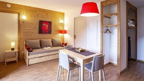 A compact room with a wooden wall, a sofa, a dining table with chairs, a hanging lamp, and a wardrobe. - Hameau 6 002 - SPA & PISCINE studio 4 pers. (Orelle)