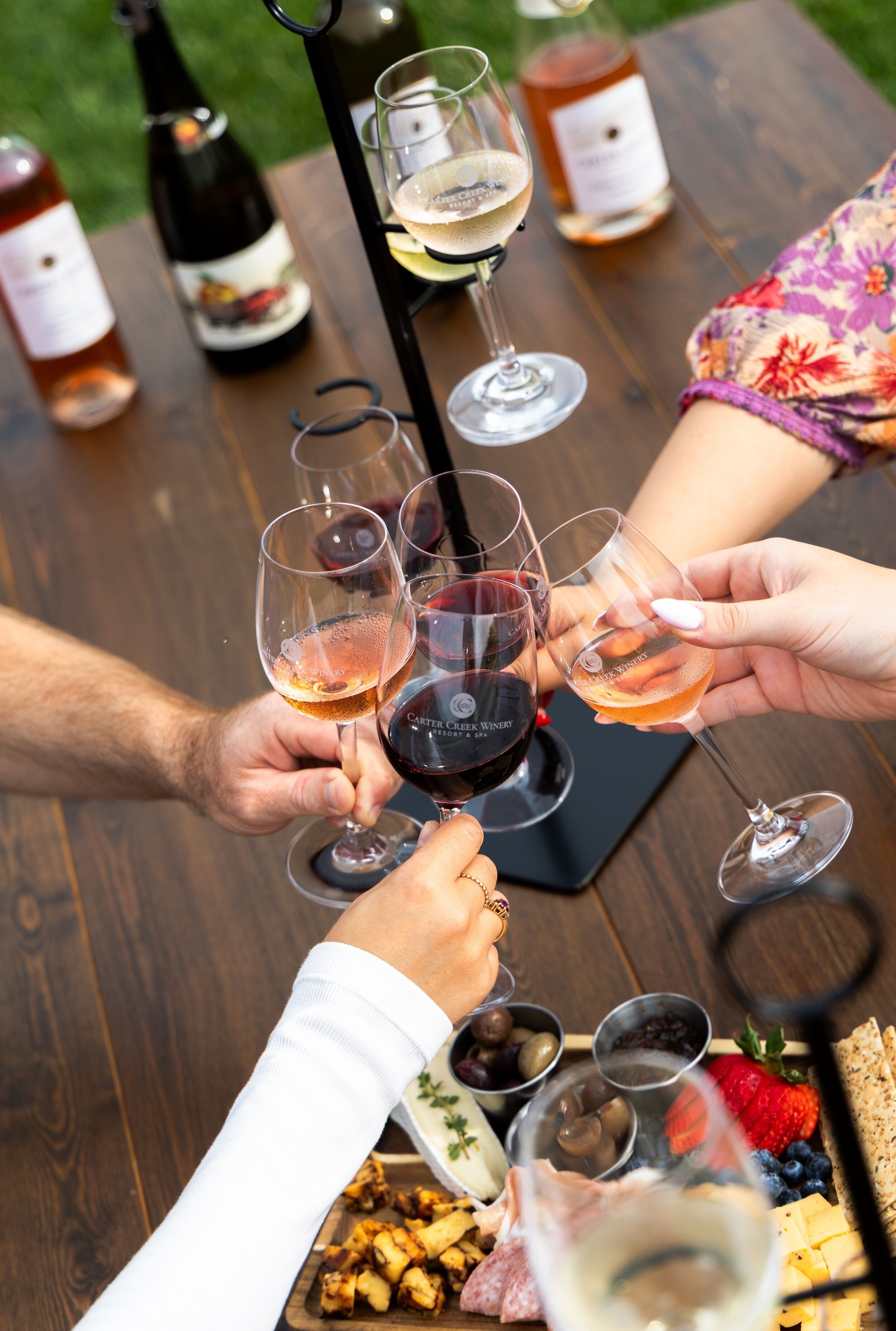 Un grupo de personas brindando con copas de vino en una mesa de madera con una variedad de quesos, frutas y aceitunas.