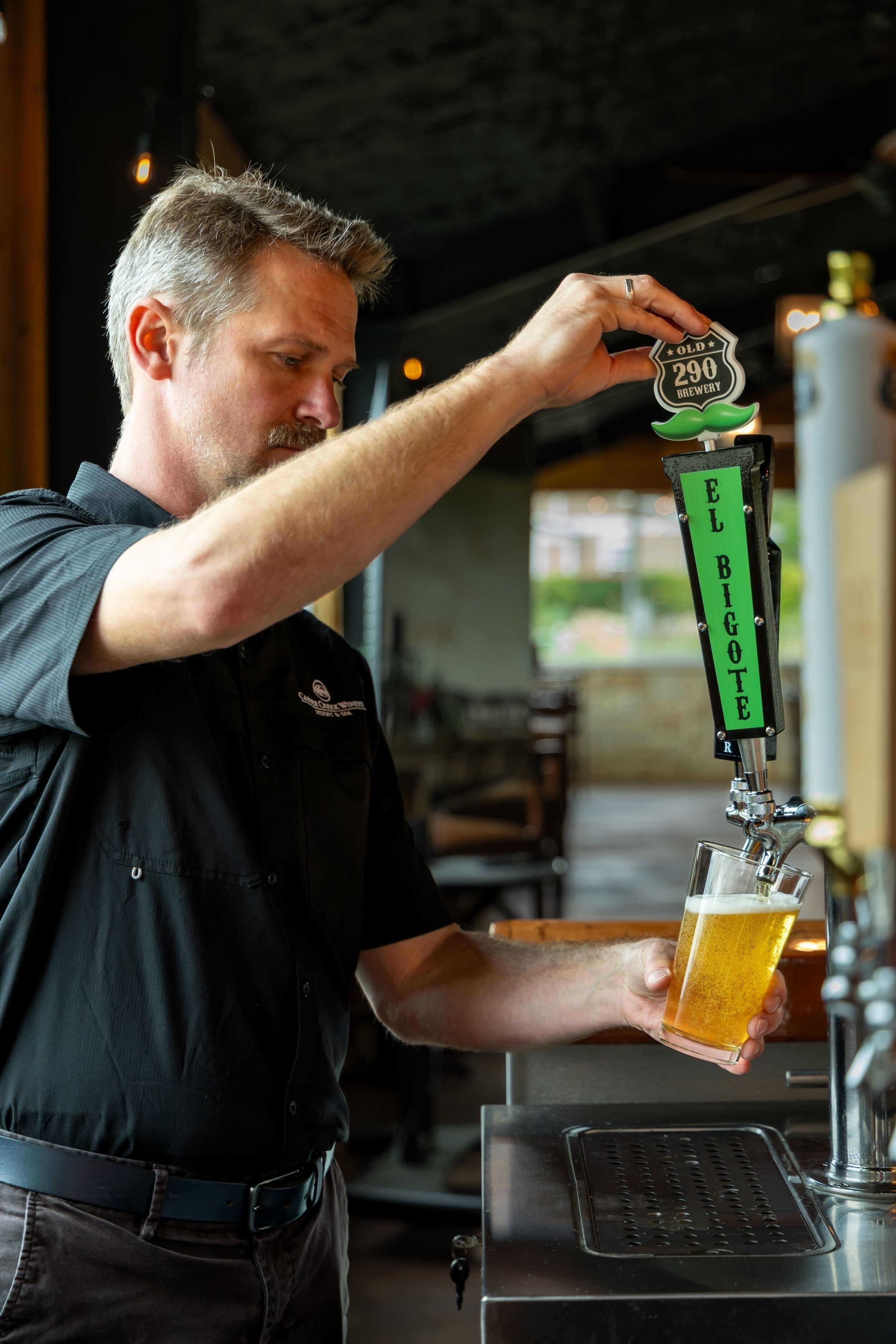 A person pouring beer from a tap labeled 'EL BIGOTE' into a glass.