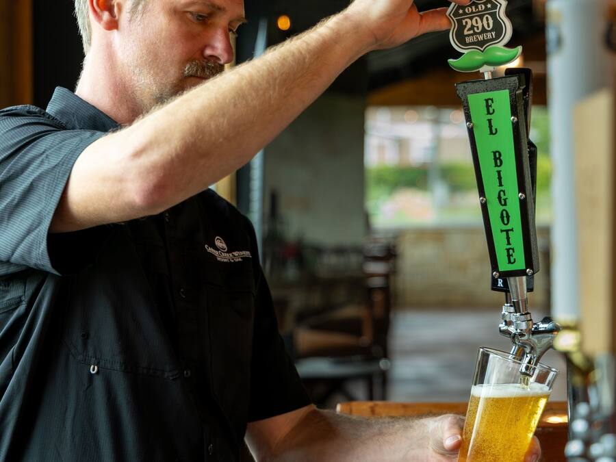A person pouring beer from a tap labeled 'EL BIGOTE' into a glass.