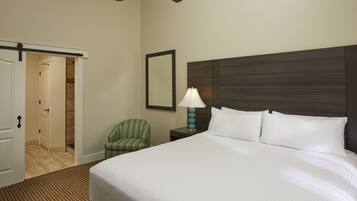 Una habitación de hotel con una cama grande, una mesita de noche con lámpara, una silla y una puerta que da a un baño.