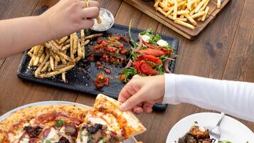 Uma mesa de jantar com pizza, hambúrguer, batatas fritas, salada e um copo de cerveja.