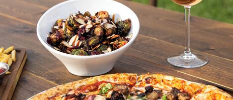 A pizza and a bowl of food on a wooden table.