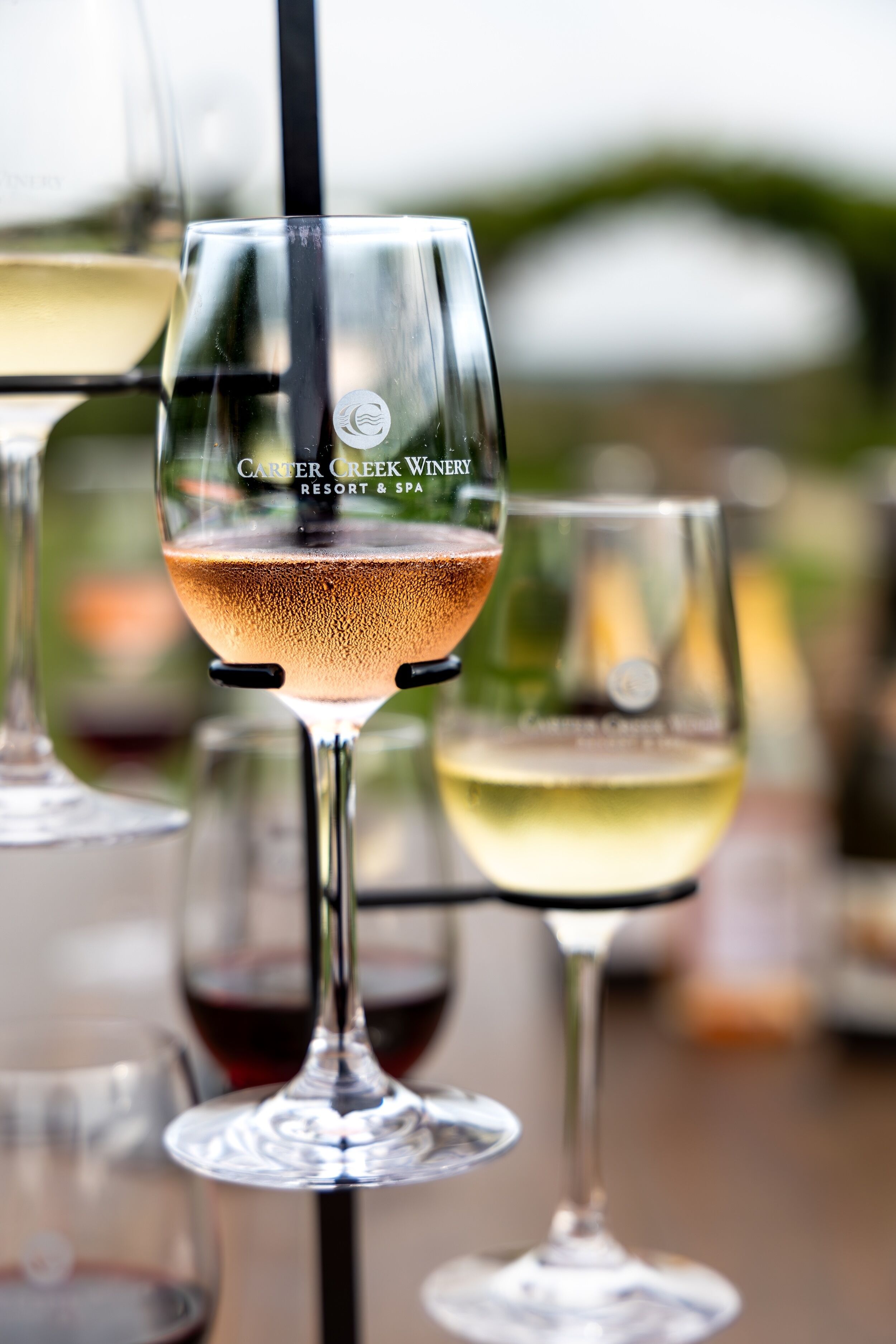 A glass of rosé wine with a black straw, surrounded by other wine glasses.