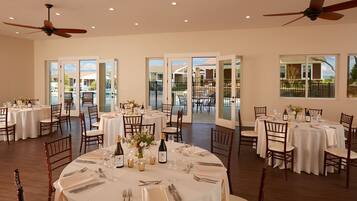 A spacious dining area with multiple round tables set for a formal meal, featuring elegant table settings and a view of the outdoor patio.