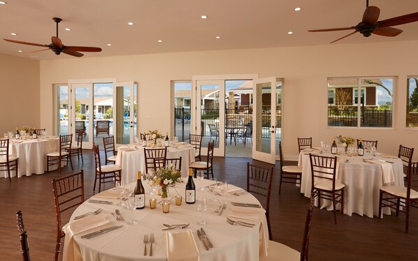 Un comedor amplio con varias mesas redondas dispuestas para una comida formal, con elegantes vajillas y vistas al patio exterior.