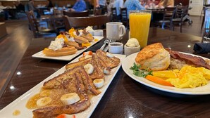 Un buffet de petit-déjeuner proposant divers plats, notamment des crêpes, des gaufres, des œufs et du jus d’orange.