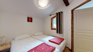 A bedroom with two beds, a window with curtains, a radiator, and a picture on the wall.