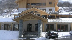 A two-story wooden building with a stone base, a balcony on the upper floor, and a snow-covered roof.