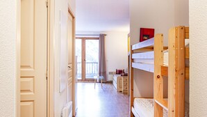 Un pasillo estrecho con literas de madera a la derecha, una puerta a la izquierda y una vista de un balcón en la distancia.
