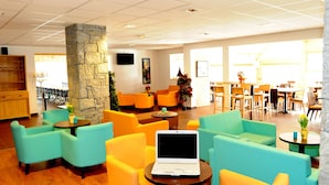 A spacious lobby with teal and yellow seating, a stone pillar, and a laptop on a table. - Hameau 8 201 - SPA & PISCINE studio 4 pers. (Orelle)