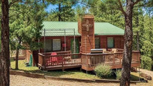 A cabin with a deck, a chimney, and a green roof. - Hilltop Cabin (Ruidoso)