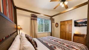A bedroom with a bed, a window with curtains, a ceiling fan, a wooden wardrobe, and a wall-mounted picture. - Hilltop Cabin (Ruidoso)