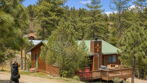 A cabin with a deck, surrounded by pine trees. - Hilltop Cabin (Ruidoso)