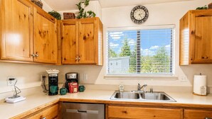 A kitchen with wooden cabinets, a stainless steel sink, a coffee maker, and a dishwasher. - Hilltop Cabin (Ruidoso)
