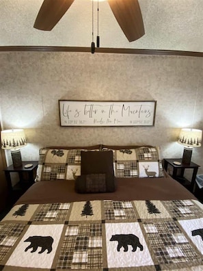 A bedroom with a bed, a headboard, two bedside tables, and a wall-mounted sign.