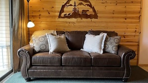 Un canapé en cuir marron avec des coussins à motifs, placé contre un mur en bois orné d’une silhouette de montagne et d’animaux sauvages.