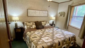 Une chambre avec un lit, un ventilateur de plafond, un panneau fixé au mur, une fenêtre avec des stores et une table de chevet avec une lampe.