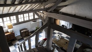Una habitación con suelo a cuadros, vigas de madera, una escalera, una mesa con lámpara y un radiador.