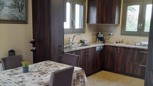 Una cocina con armarios de madera oscura, una mesa de comedor con mantel estampado y una ventana con vista a follaje.