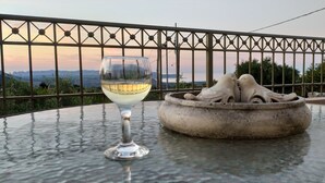 Una copa de vino blanco sobre una mesa, con un cuenco decorativo y una baranda de metal al fondo.