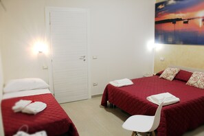 A hotel room with two beds, each with a red quilted bedspread and white pillows. There is a white chair in the room, and a door is visible in the background. - Aden B&B Salento (Sannicola)