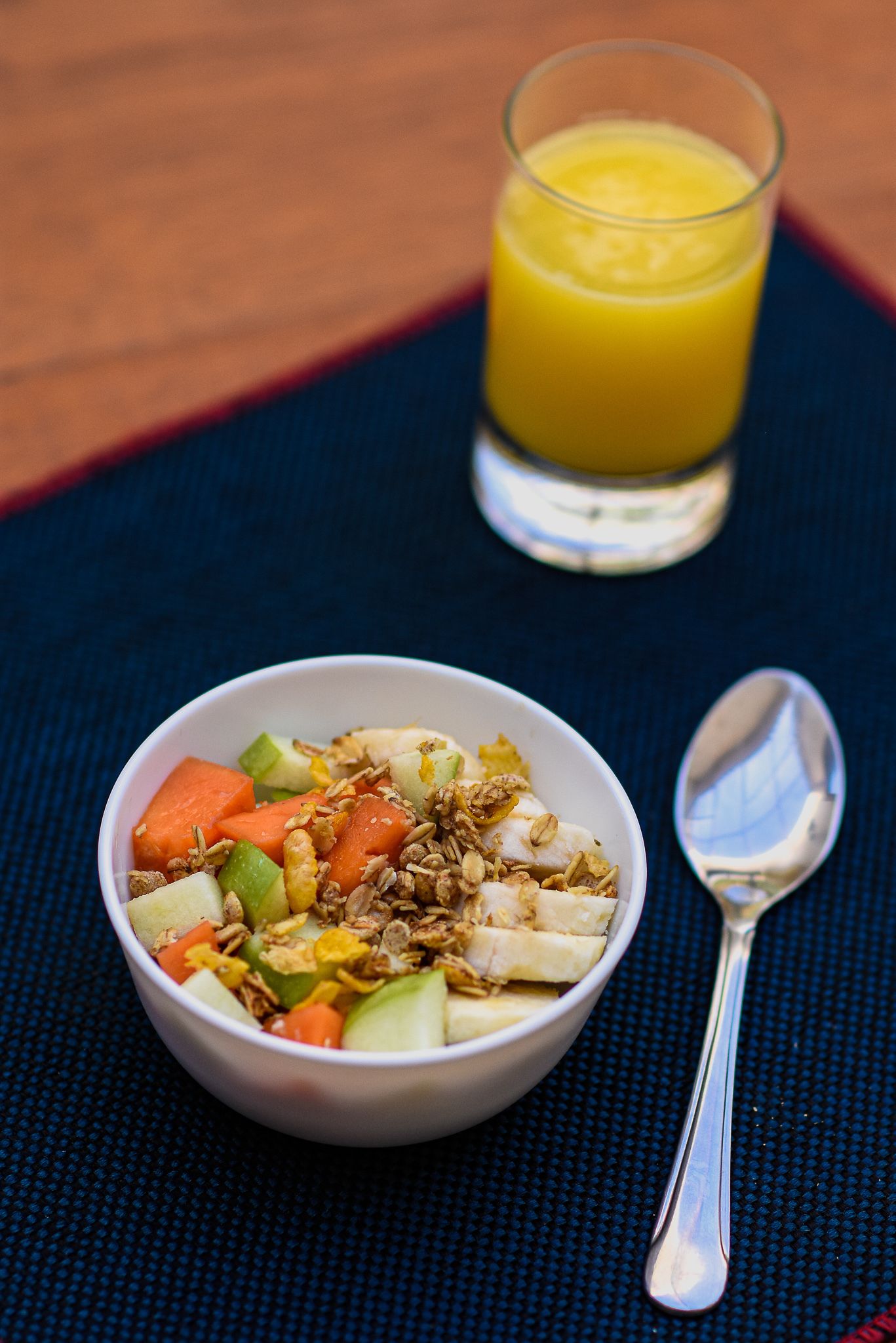 A bowl of fruit salad with granola and a glass of orange juice on a table.