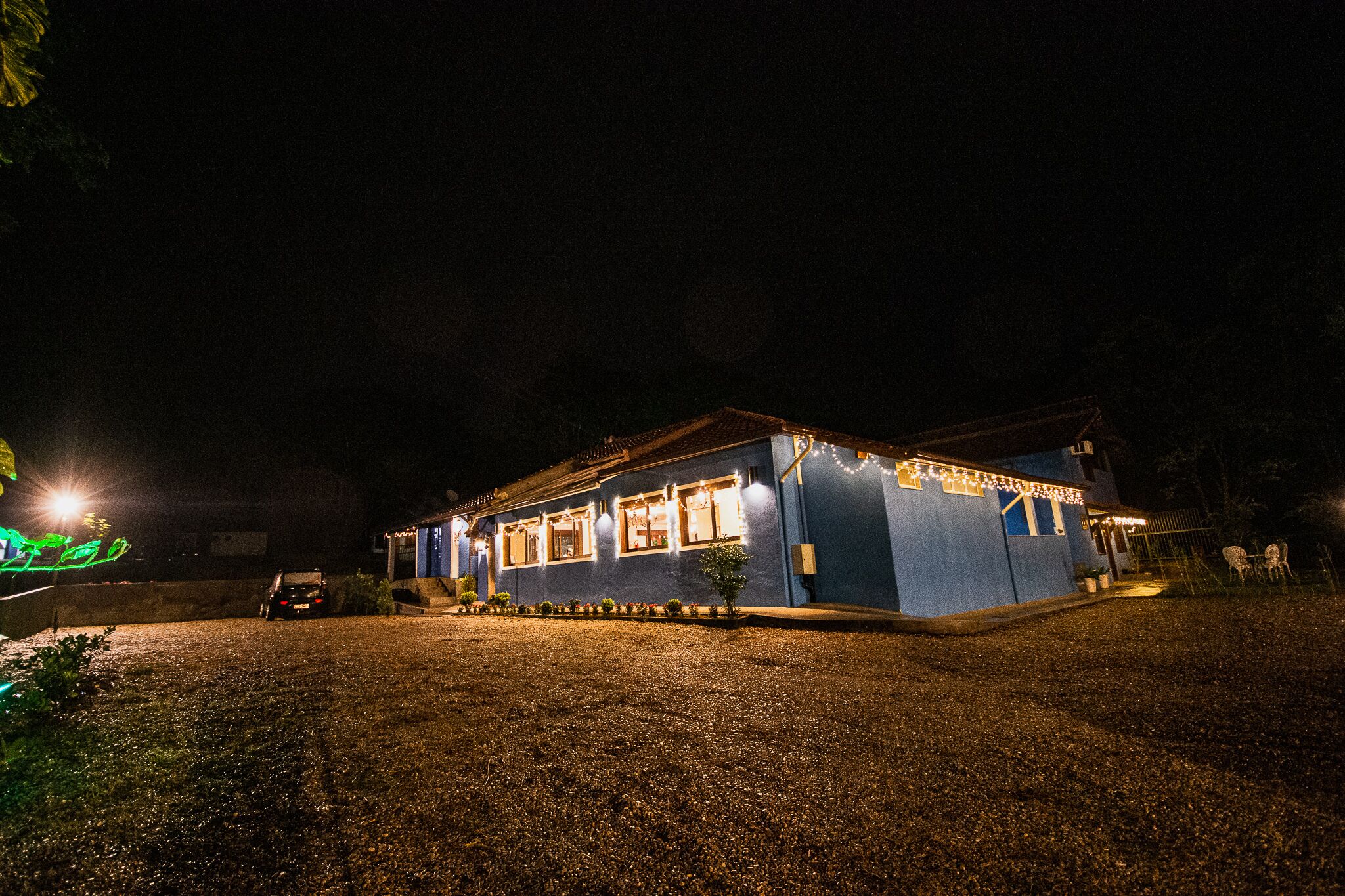 A house with a gravel driveway, a car parked in front, and string lights along the roof.