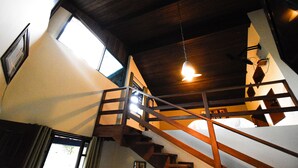Una escalera de madera con barandal de metal que sube a un segundo piso. En el centro del techo, hay una lámpara colgante.