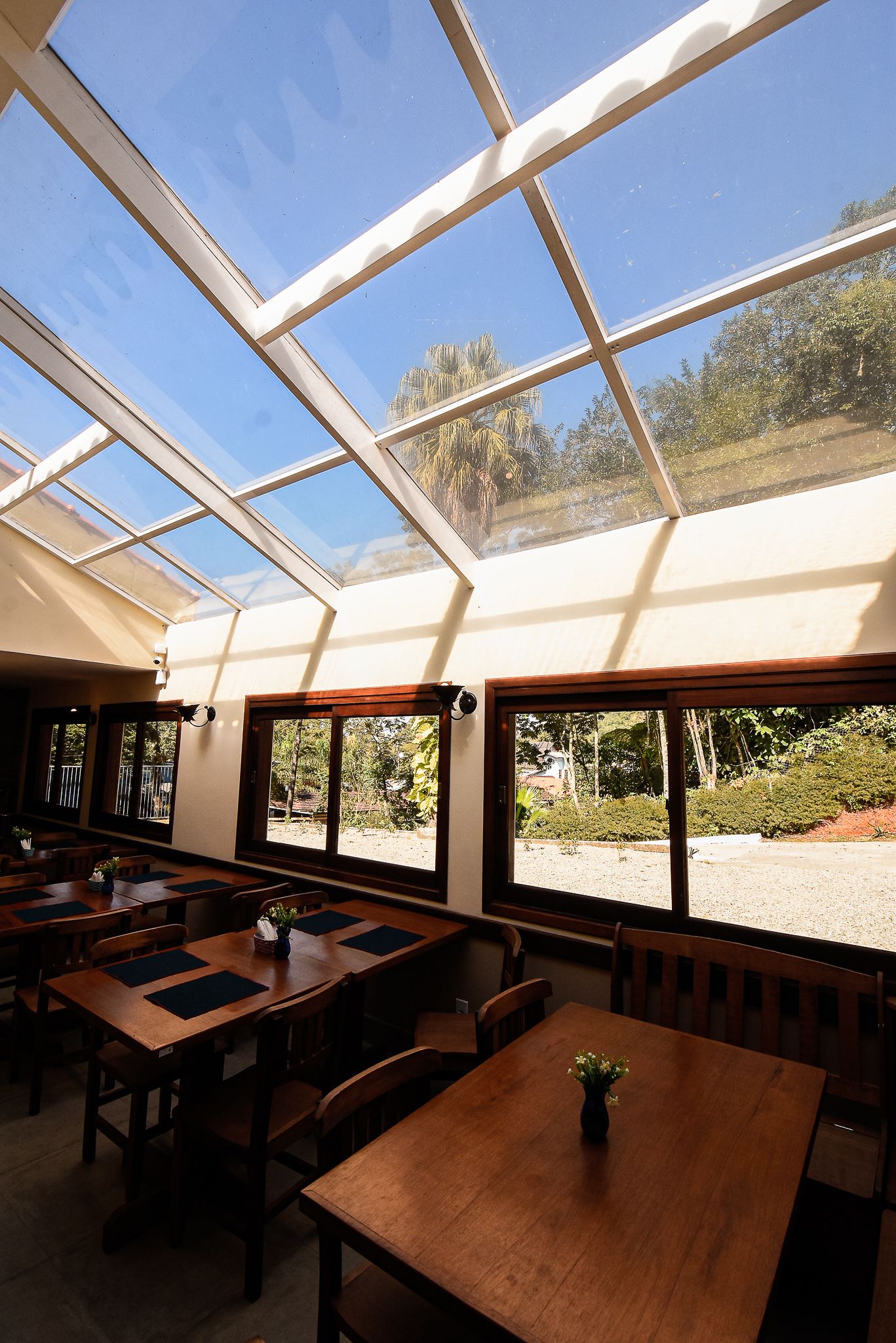 Un restaurante con amplios ventanales y techo de cristal, mesas y sillas de madera.
