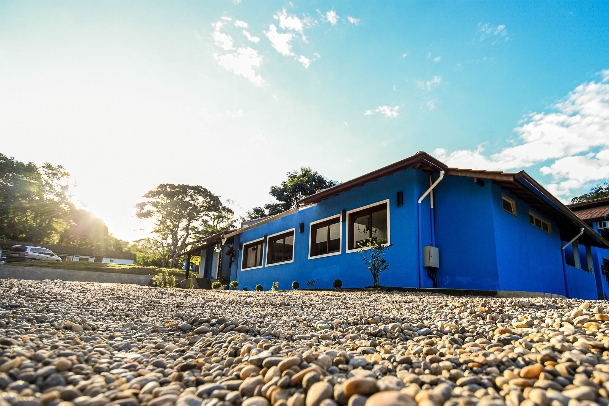 A blue building with a sloped roof and multiple windows, surrounded by a gravel driveway.