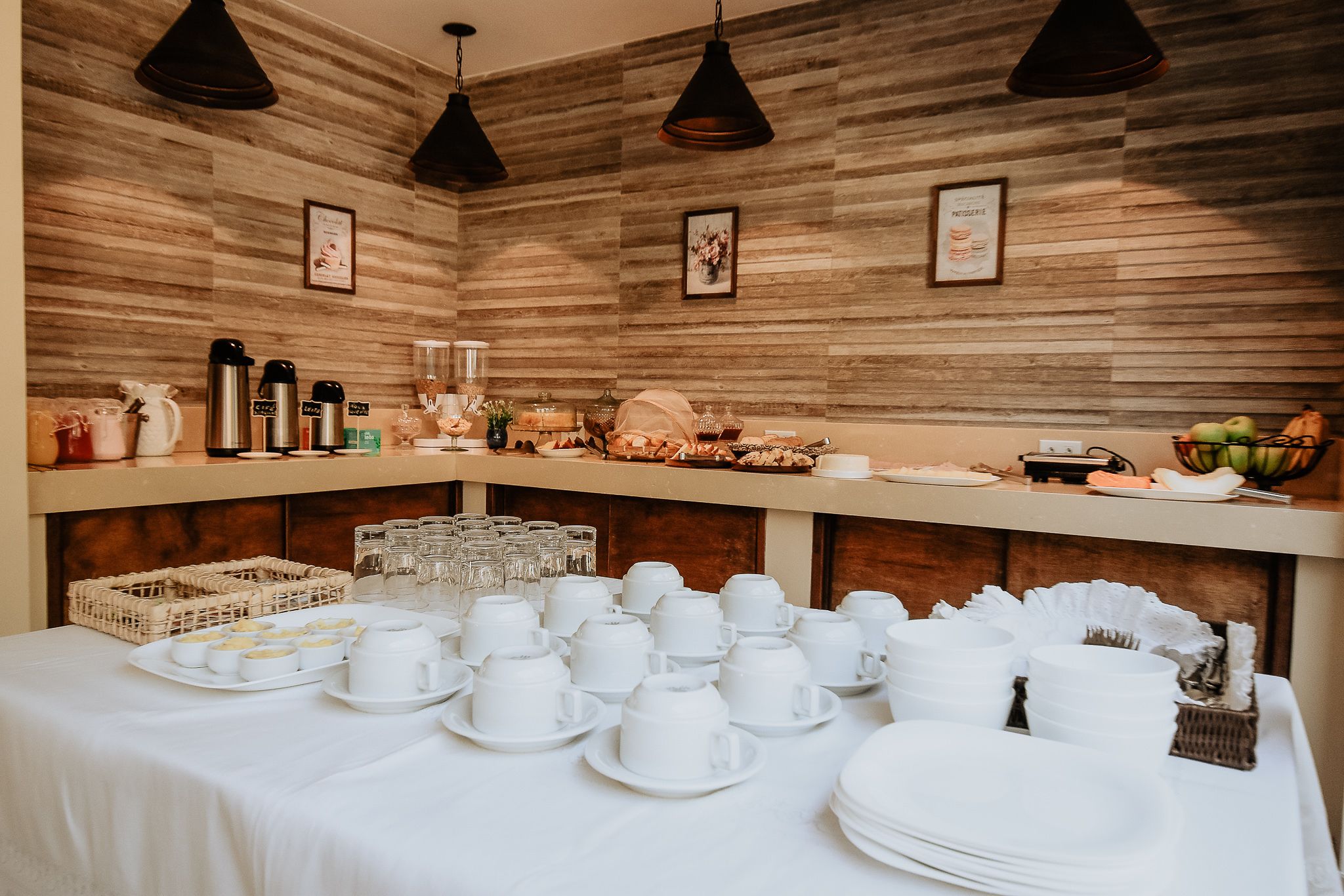 A buffet setup with white dishes and cups, a wicker basket, and a fruit bowl.