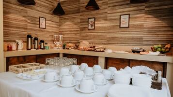 A buffet setup with white dishes and cups, a wicker basket, and a fruit bowl.