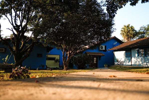 A residential area with blue houses, a large tree, and a clear sky. - Pousada Paris Hostelli (Itatiaia)