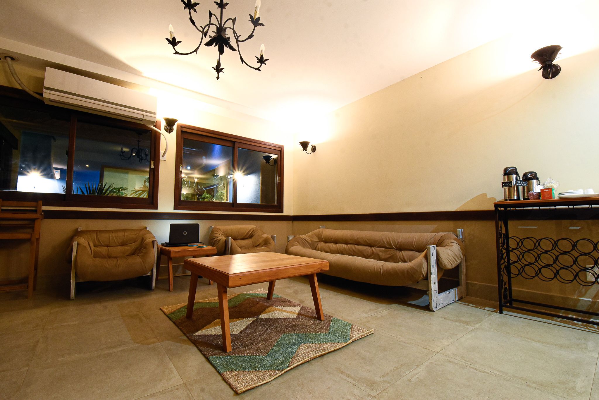A living room with a sofa, two armchairs, a wooden coffee table, a rug, a TV, and a kitchen area with a refrigerator and coffee machine.