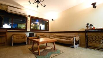 A living room with a sofa, two armchairs, a wooden coffee table, a rug, a TV, and a kitchen area with a refrigerator and coffee machine.