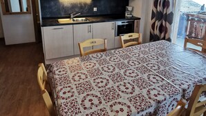 A compact kitchen with a dining area, wooden cabinets, a black countertop, and a table with a floral tablecloth.