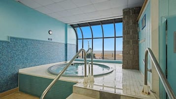 An indoor swimming pool with a view of the beach, a clock on the wall, and a tiled floor.