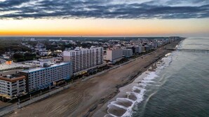 Eine Küstenstadtlandschaft mit einem Hotel am Strand, einer Pier und einem Sonnenuntergang.