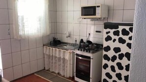 Eine kleine Küche mit weißen Fliesen, einer Mikrowelle, einem Herd und einem Kühlschrank mit Kuhmuster.