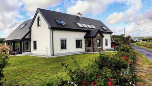 Ein zweistöckiges Haus mit geneigtem Dach, zahlreichen Fenstern und einem gepflegten Rasen mit blühenden Pflanzen.